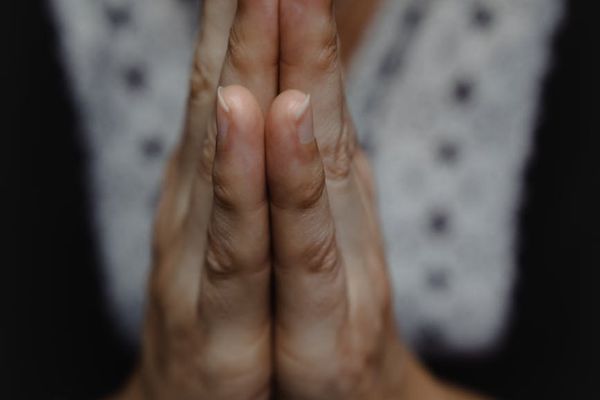 Yoga practitioner hands in a mudra position against a dark background.